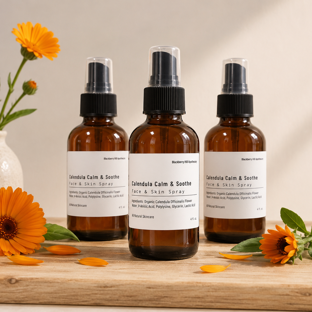 Three amber glass spray bottles labeled Calendula Calm & Soothe Face & Skin Spray, arranged on a wooden surface with orange flowers and green leaves against a warm beige background.