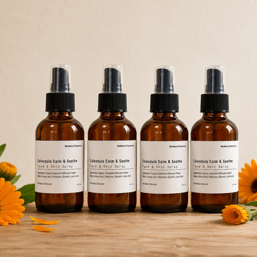 Four amber glass spray bottles labeled 'Cannabis Cain & Scent' arranged on a wooden surface with orange flowers around them against a warm beige background.