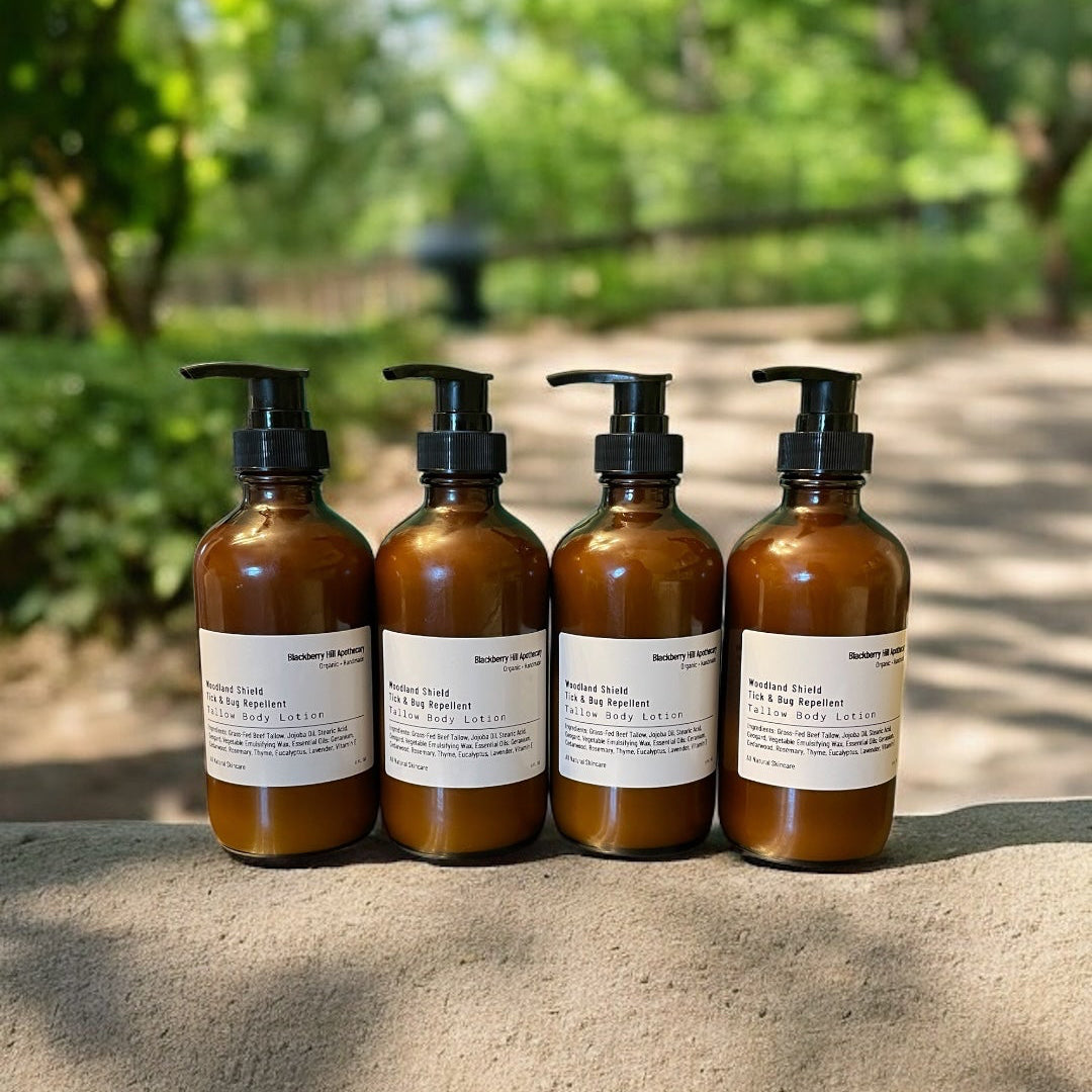 Four amber glass pump bottles with black dispensers and white labels, lined up on a stone surface outdoors with a blurred green forest background.
